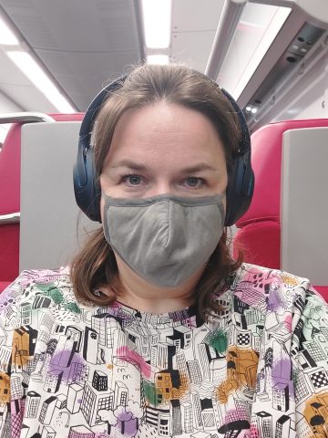 Daniela im Zug mit Kopfhörern und Maske